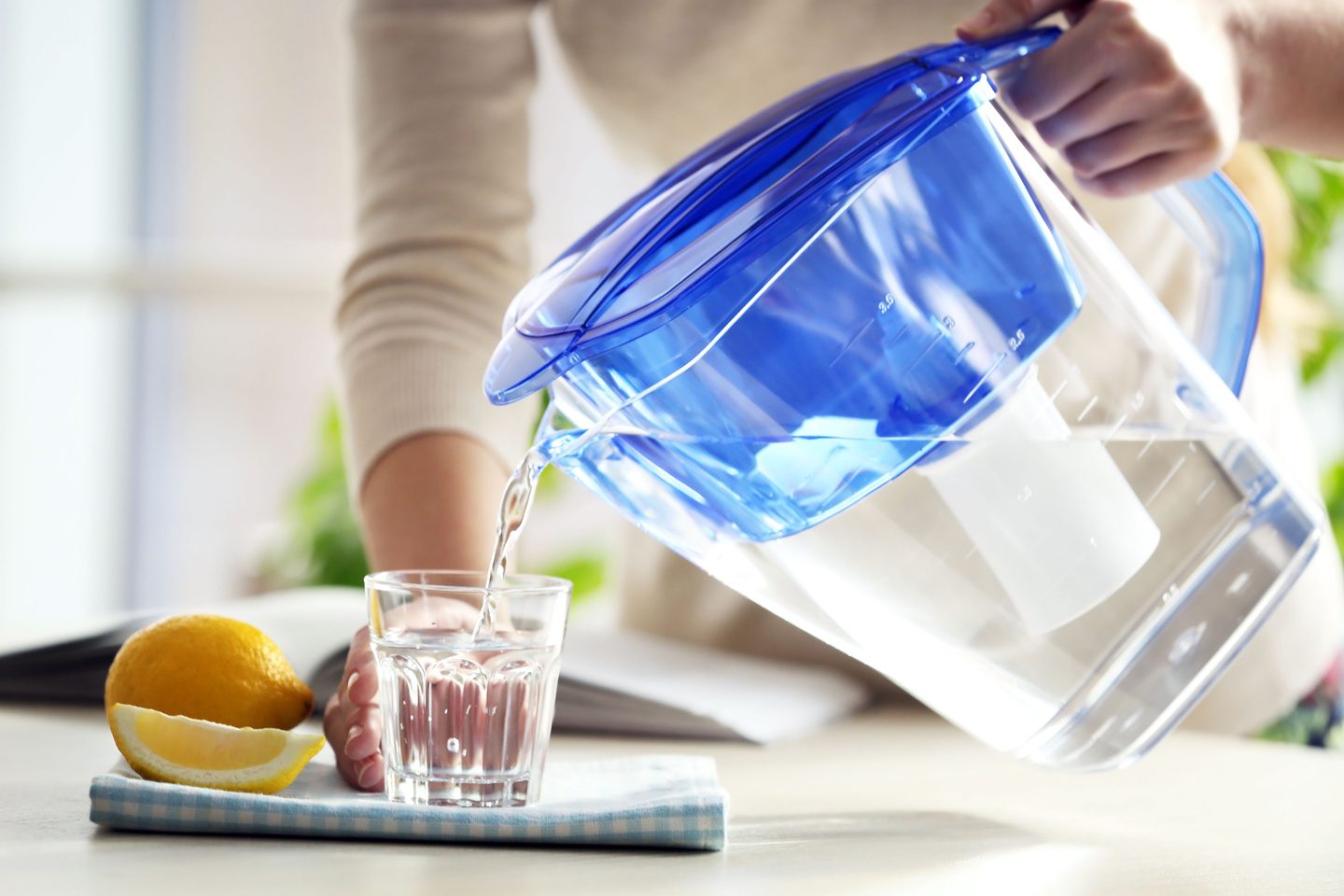 Woman pouring filtered water from jug into glass in the kitchen