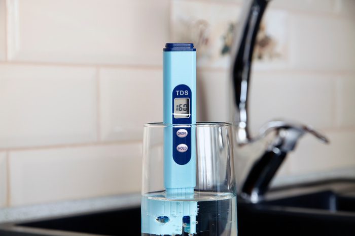 Electronic pH meter in a glass of water. In the background there is a tap for drinking water. The concept of testing water for miralization. Water test of hard water and soft water