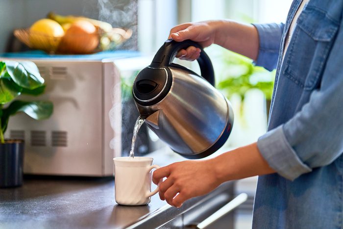 Female hands pouring boiling water from a modern metal stainless kettle in a glass cup