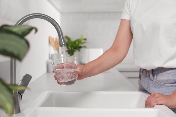Woman filling glass with water from tap in kitchen