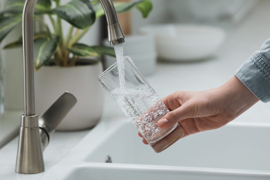 Woman filling glass with purified water from tap in kitchen